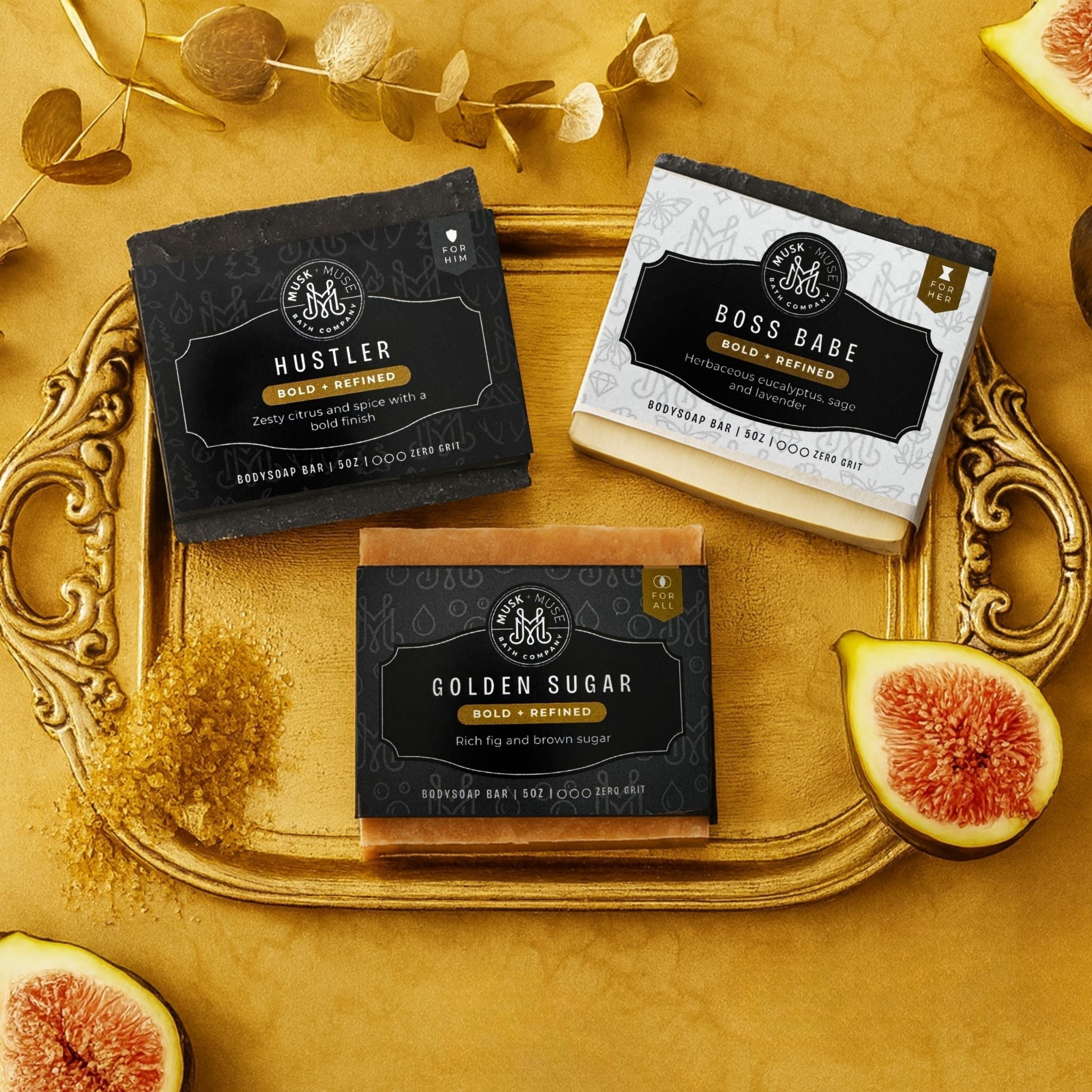 Bold and Refined set of three barsoaps for him and her on a gold tray surrounded by gold eucalyptus, figs and turbinado sugar.